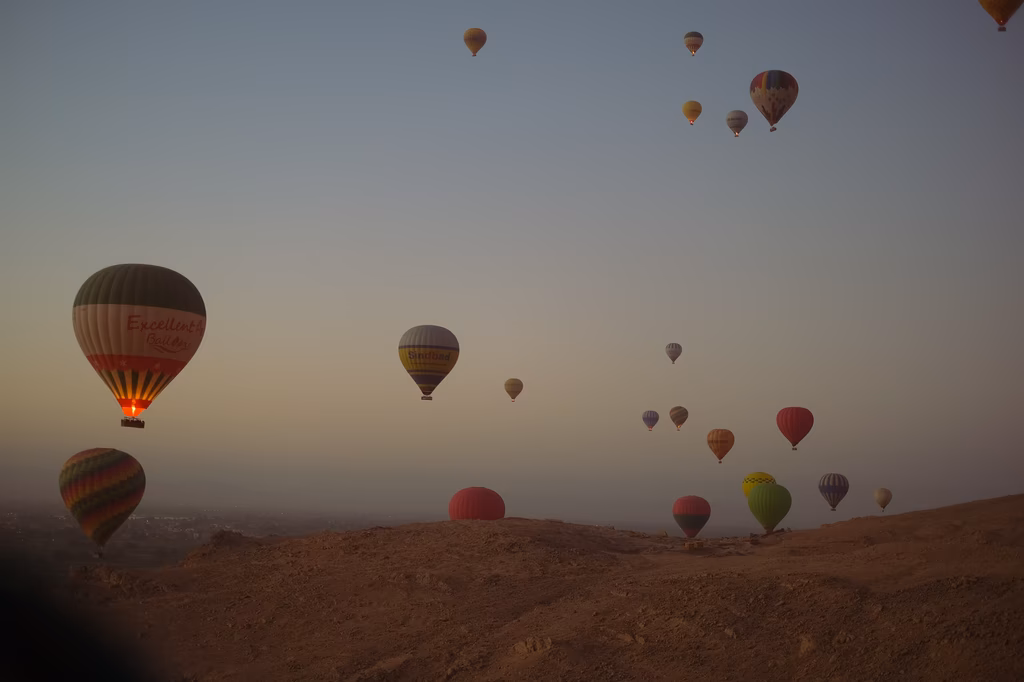 Mehrere Heißluftballons schweben über einer staubigen Wüstenlandschaft während des Sonnenaufgangs.