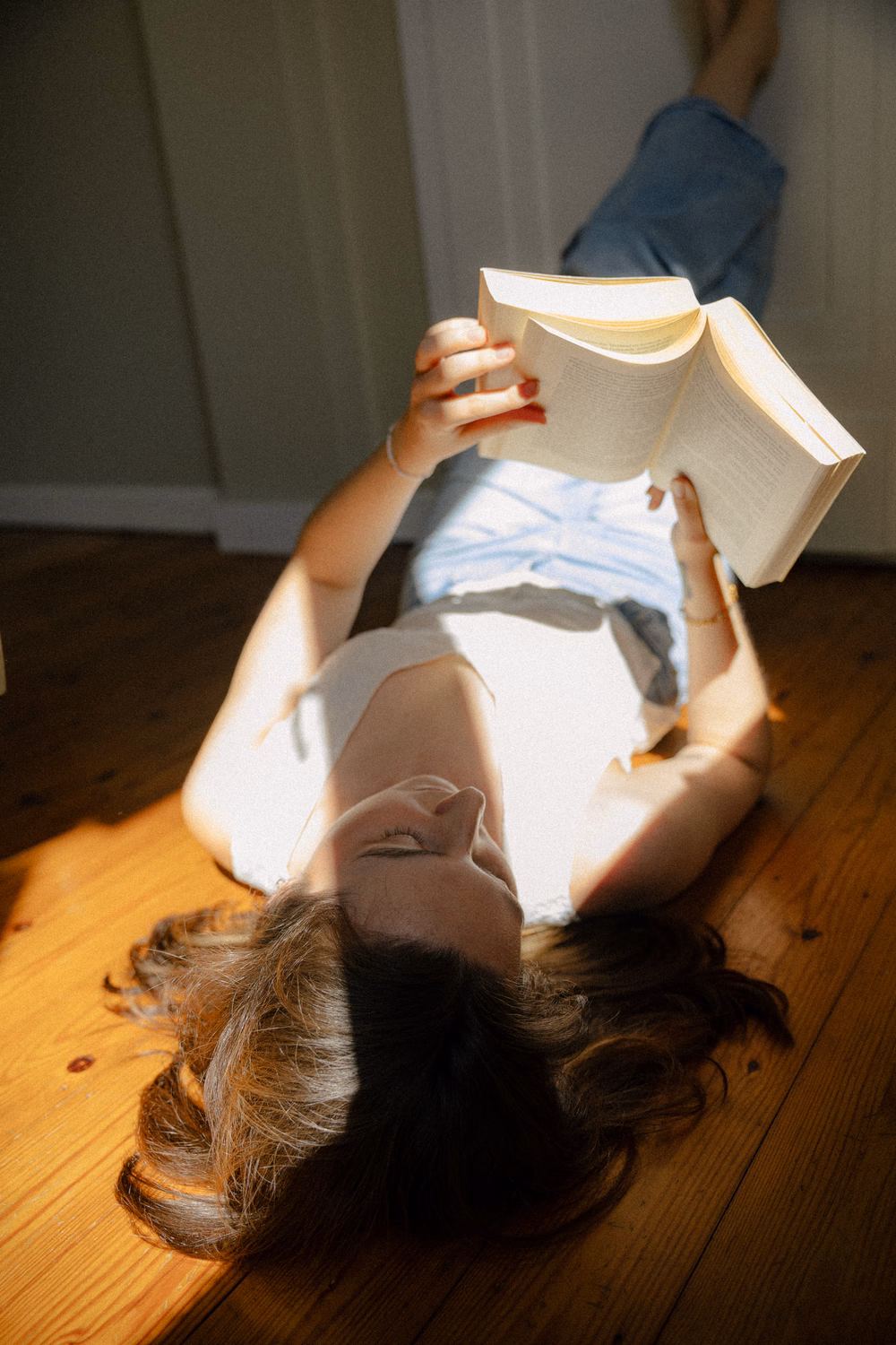 Kind liegt auf Holzboden und liest ein Buch, das Licht wirft Schatten auf das Gesicht.