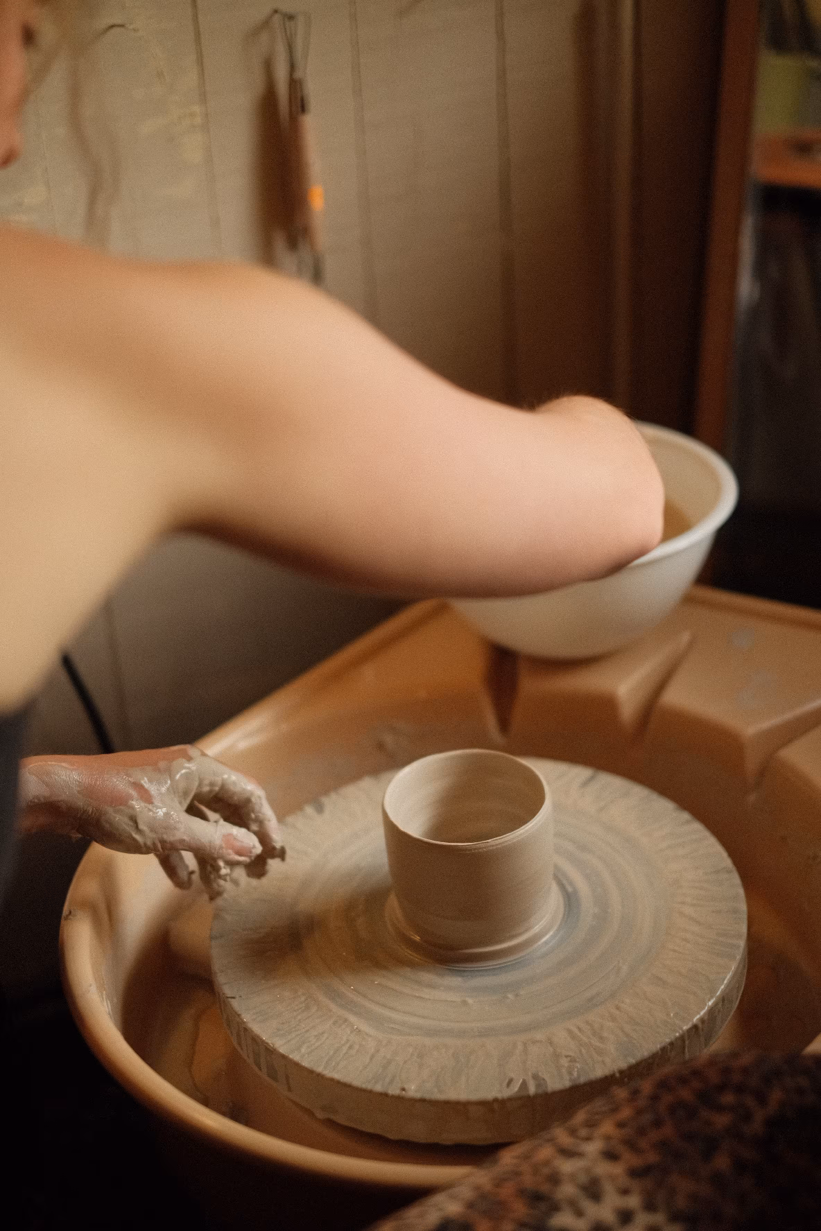 Töpfer formt Tonbecher auf Töpferscheibe, Handwerk und Keramikkunst in Werkstatt.