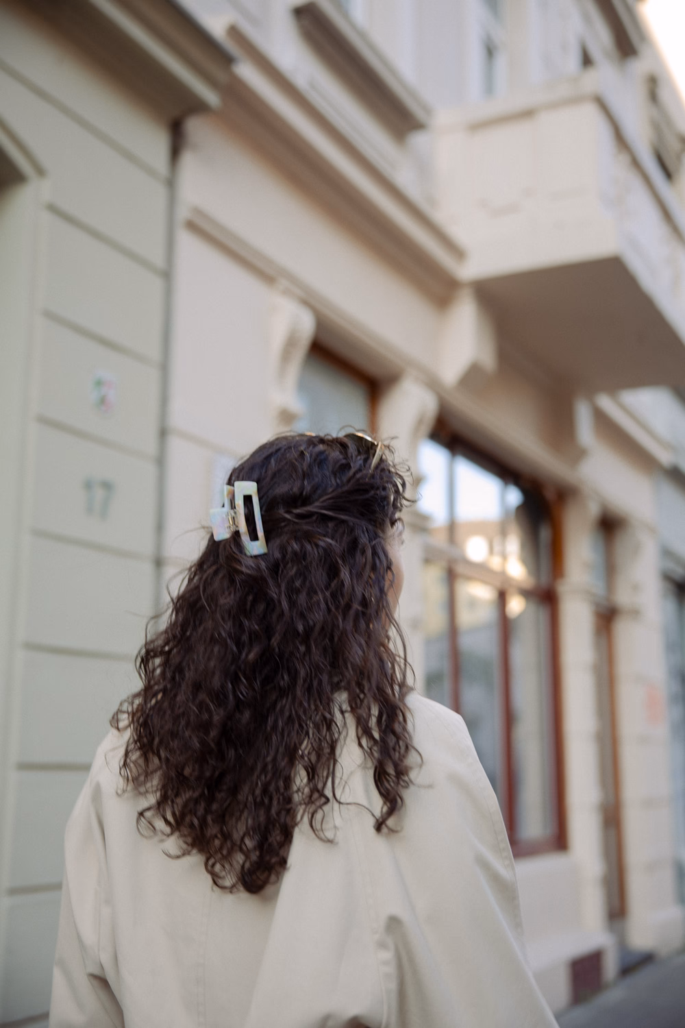 Frau mit langen dunklen Haaren und weißer Spange von hinten vor klassischem Gebäude.