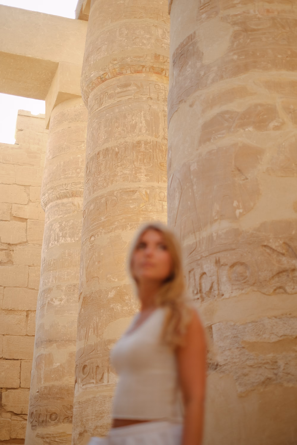 Frau in weißem Kleid vor antiken ägyptischen Säulen mit Hieroglyphen in einem Tempel.