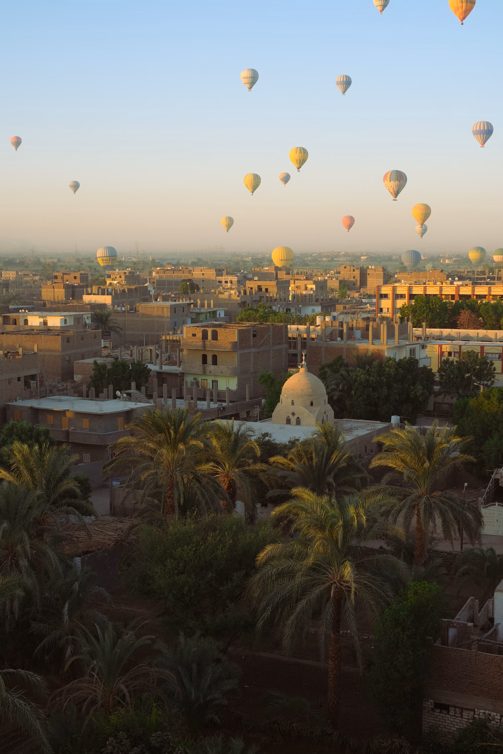Heißluftballons über Luxor, Ägypten, mit Moschee und Palmen bei Sonnenaufgang.